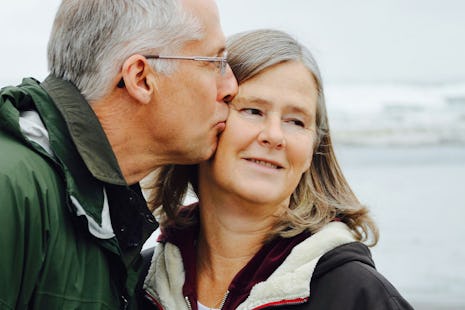 A man kisses his wife on the beach.